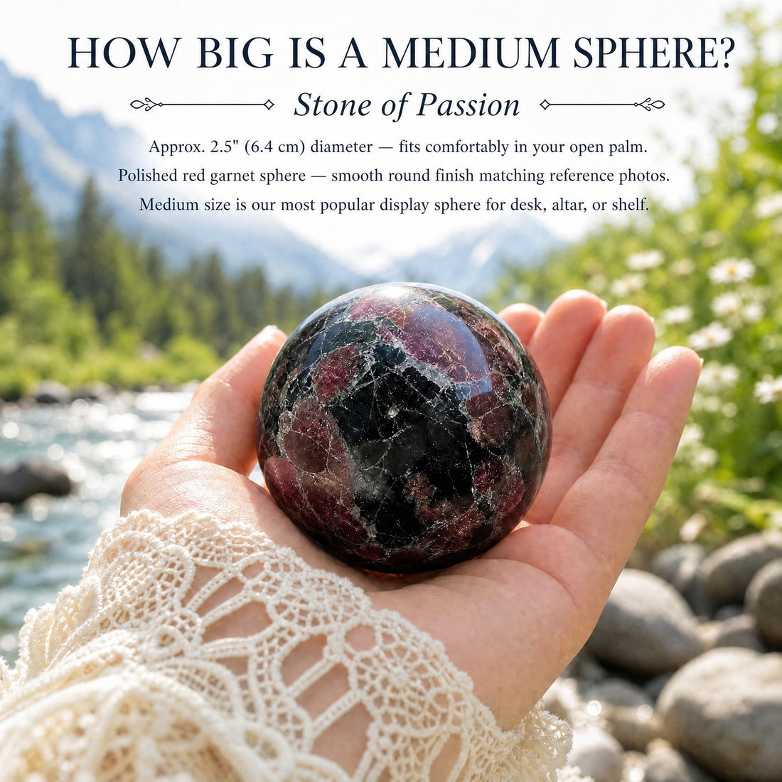 A medium red garnet sphere resting in an open palm beside a mountain stream