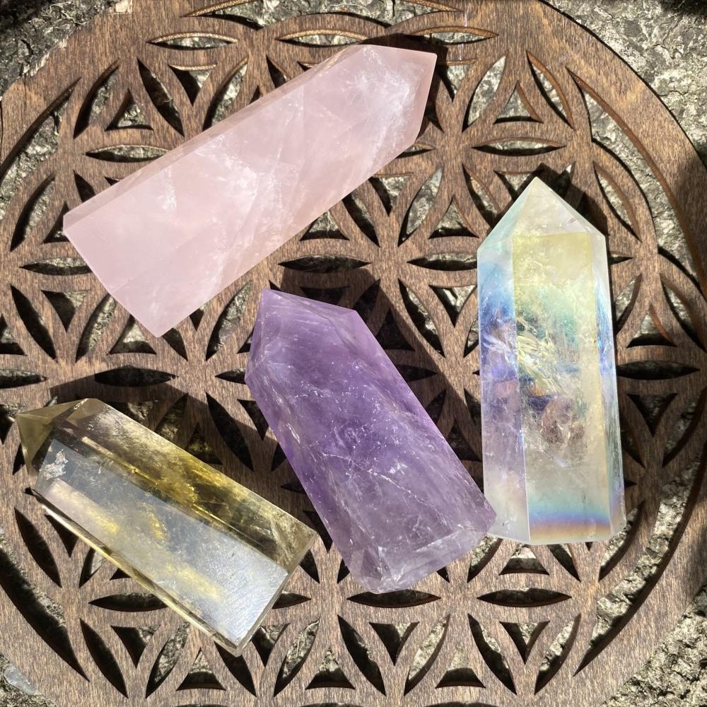 The four points lying on a wooden board seen from above: rose quartz, amethyst, citrine and a rainbow-sheened Angel Aura quartz