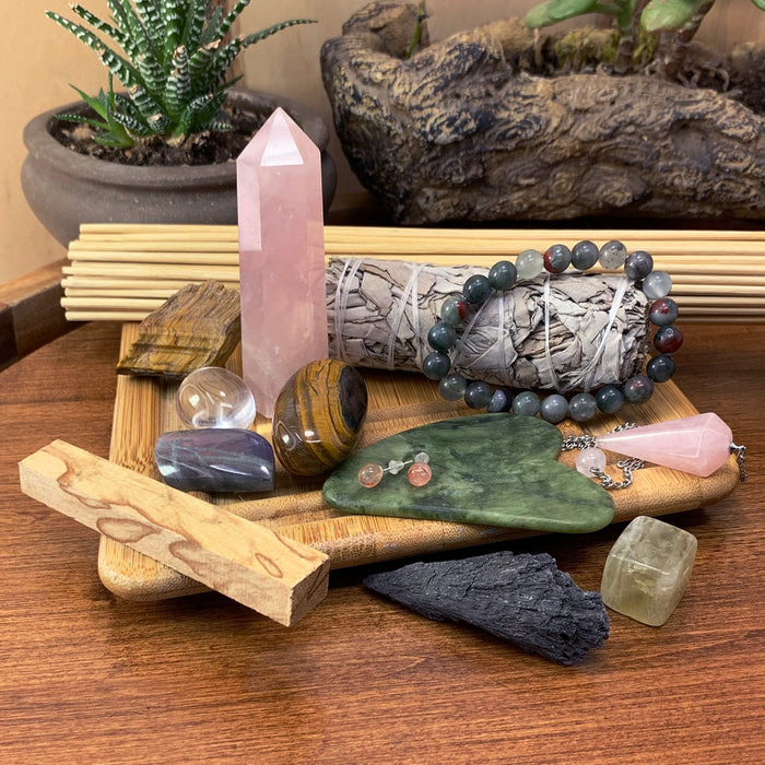 A past box with a rose quartz point, a sage bundle, palo santo sticks, a beaded bracelet, black tourmaline and polished stones