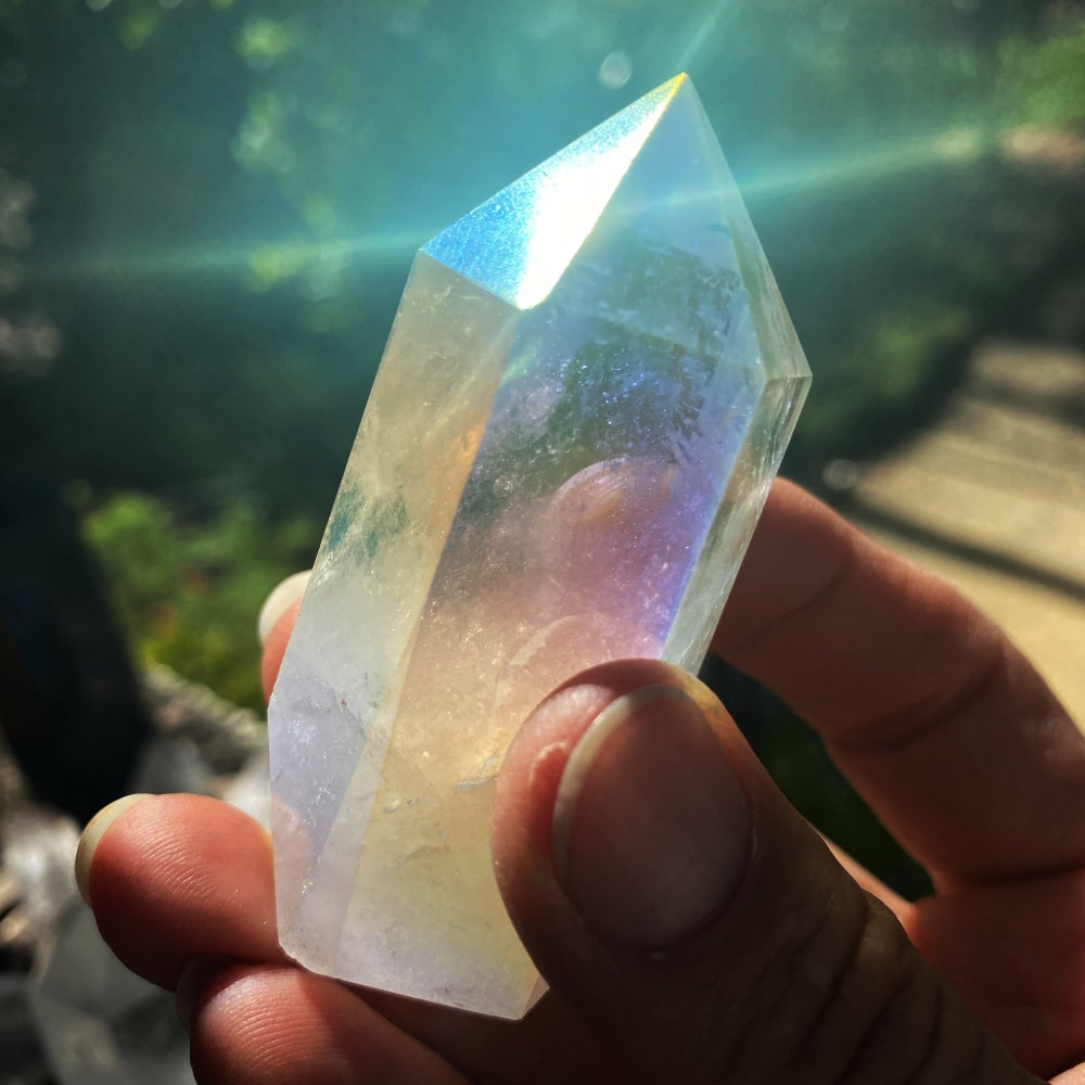 An angel aura quartz point held between fingers in sunlight, glowing with rainbow color
