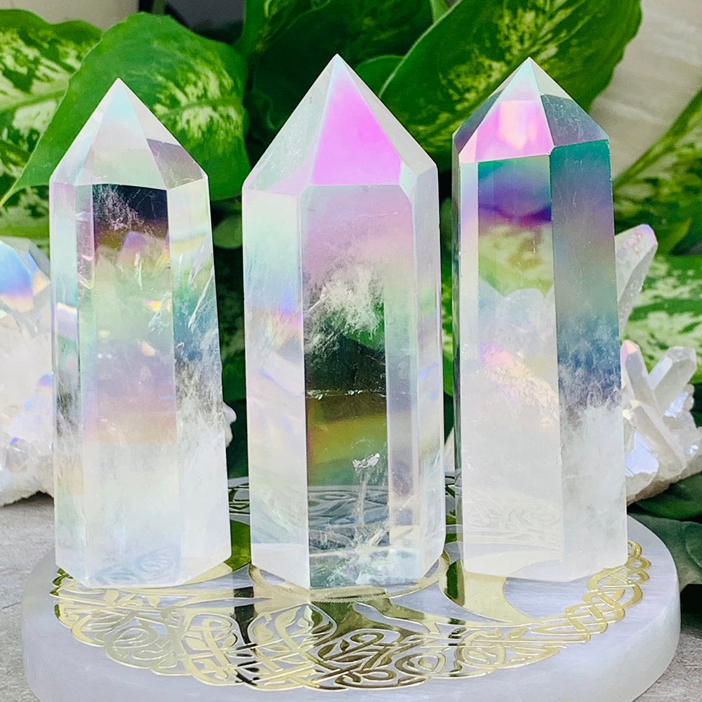 Three Angel Aura quartz points standing on a round plate, their faces shimmering pink, violet, green and blue