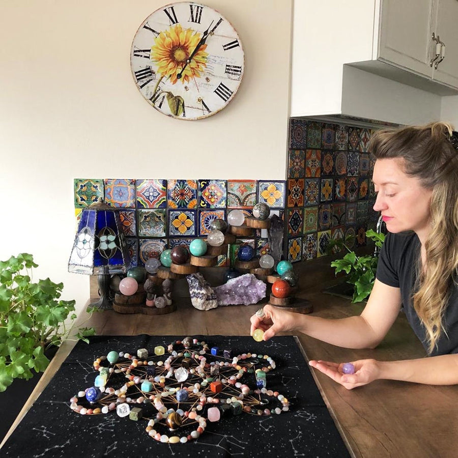 A woman placing crystal spheres on a large crystal grid laid out over the cosmic star cloth on a kitchen counter