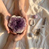 Spiritual Sleep crystal kit on cream linen with the Large Amethyst Cluster (held in two hands for scale) as centerpiece, plus lepidolite, howlite, selenite, moonstone, and smoky quartz.