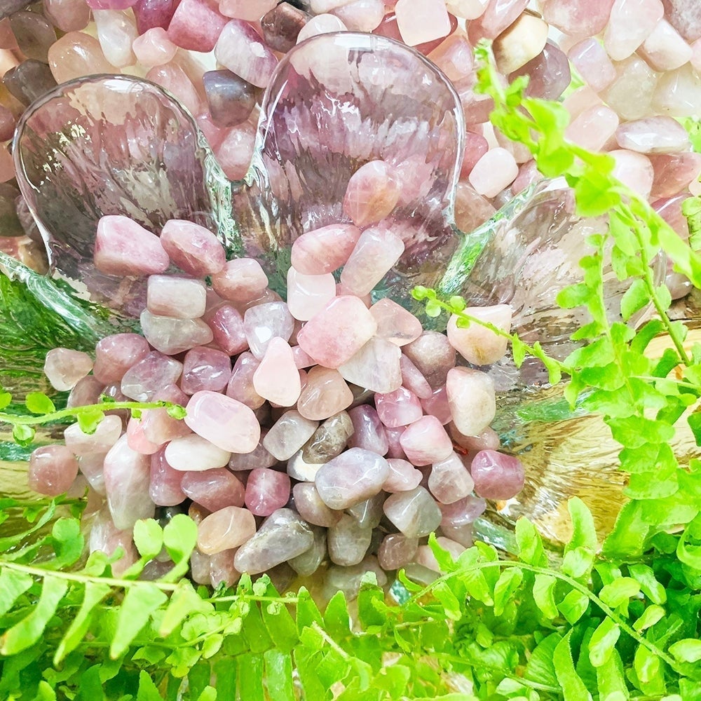 Polished Madagascar rose quartz mini gemstones in shades of rose pink and lavender, piled in a glass dish among ferns