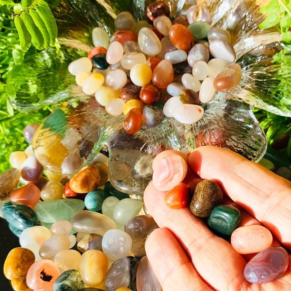 A few mixed agate mini gemstones resting on the fingers of an open hand above a glass dish of more stones