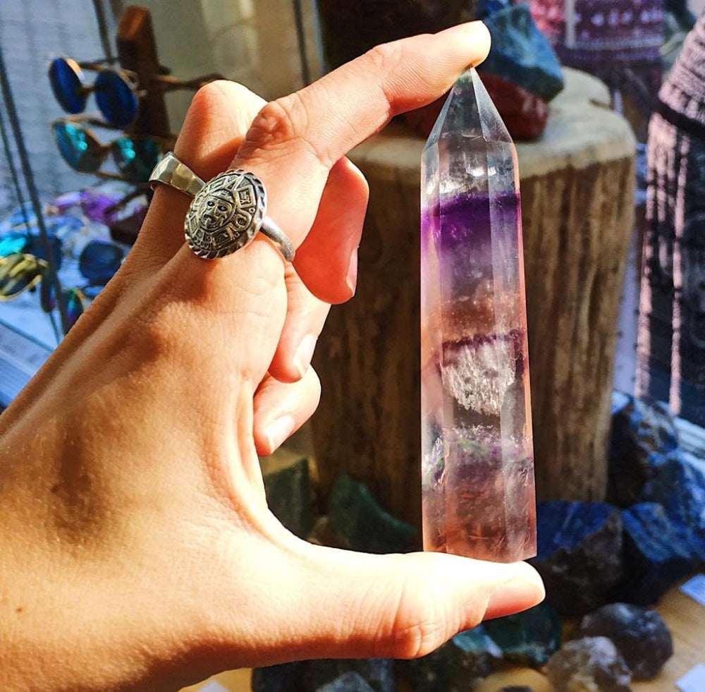 A multicolor fluorite point held between thumb and finger, showing clear and violet bands
