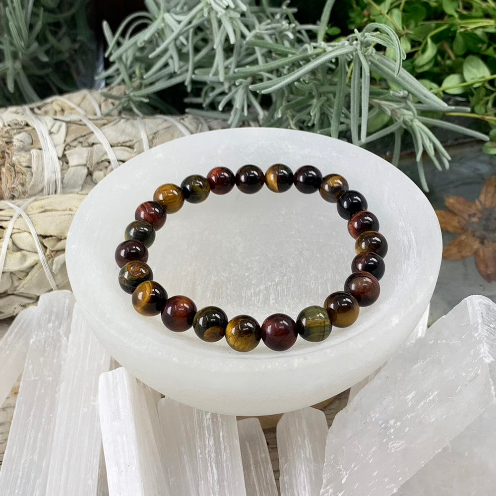 Multicolor tiger's eye mala bracelet of golden, red and blue-green beads resting in a selenite bowl