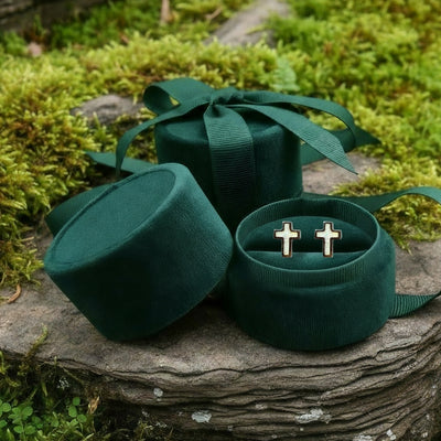The pair of opal cross earrings tucked into an open round green velvet jewelry box on a mossy stone