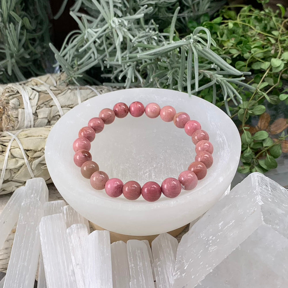 A pink rhodonite bead bracelet in rose, blush and soft brown tones resting in a selenite bowl