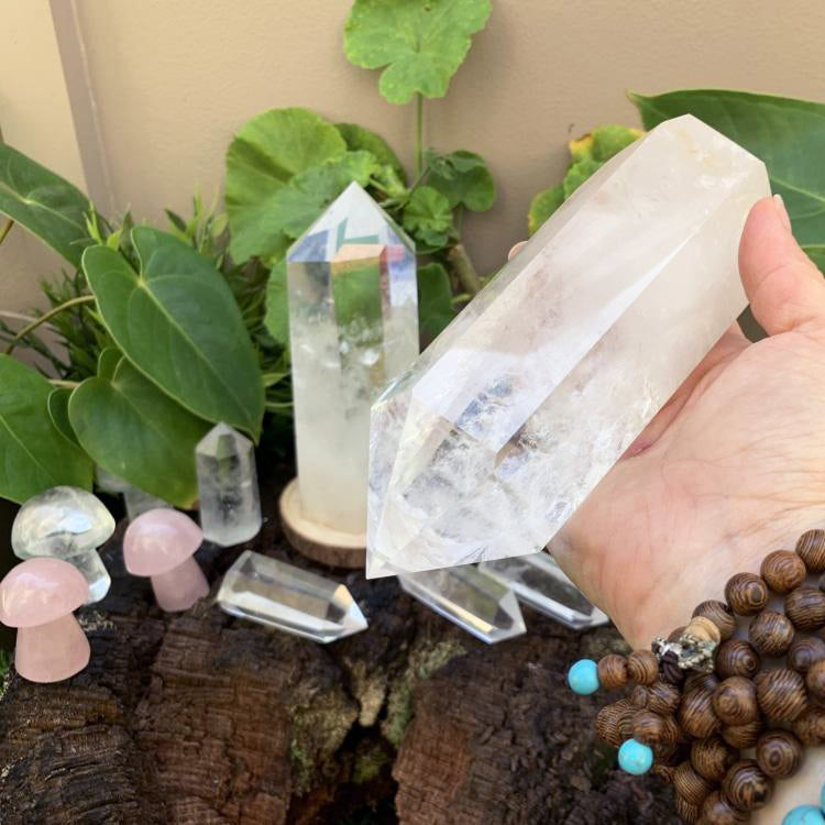 Clear quartz generator resting across an open hand beside smaller quartz points and crystal mushrooms
