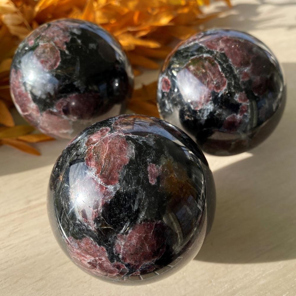Three polished red garnet spheres on a sunlit table, wine-red garnet patches set in glossy black