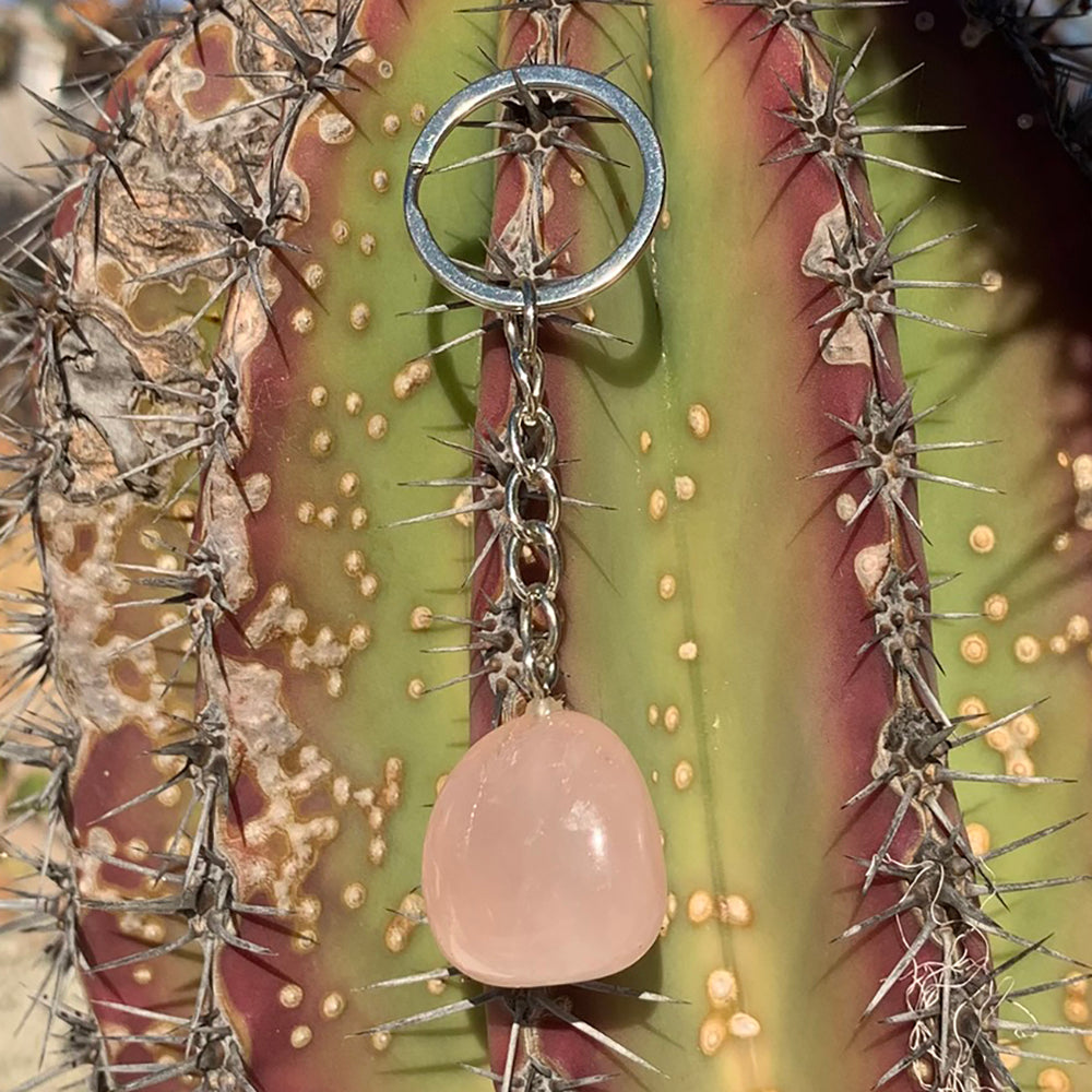 A soft pink rose quartz stone hanging from a silver-tone chain and split keyring in the sunshine