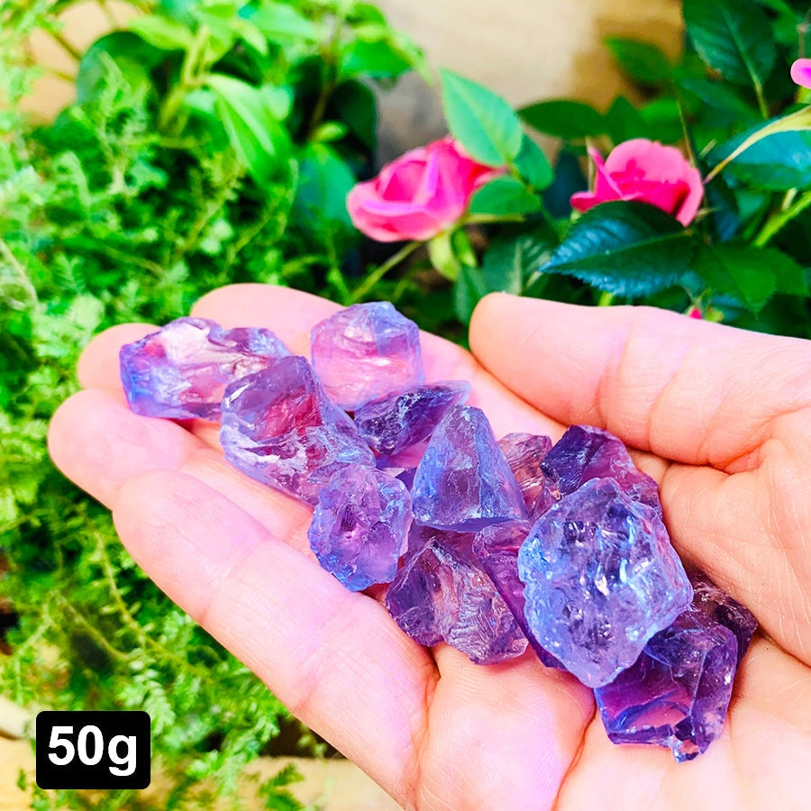A 50 gram lot of rough purple amethyst pieces resting in an open palm in front of pink roses