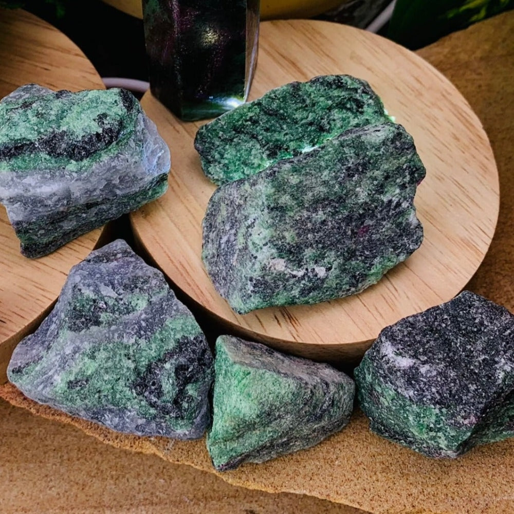 Several rough ruby in zoisite stones in shades of green, grey and black on wooden stands