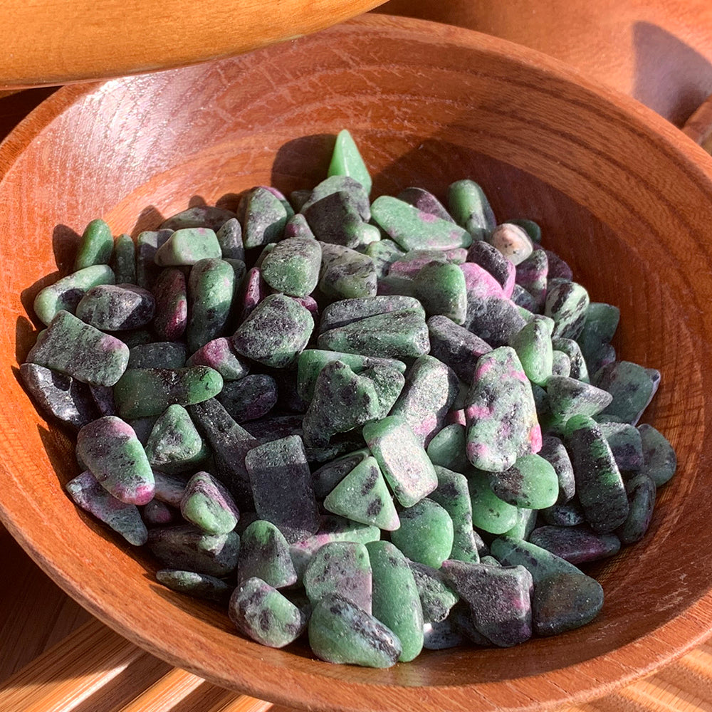A wooden bowl full of small green ruby in zoisite mini gemstones with dark flecks and pink ruby patches