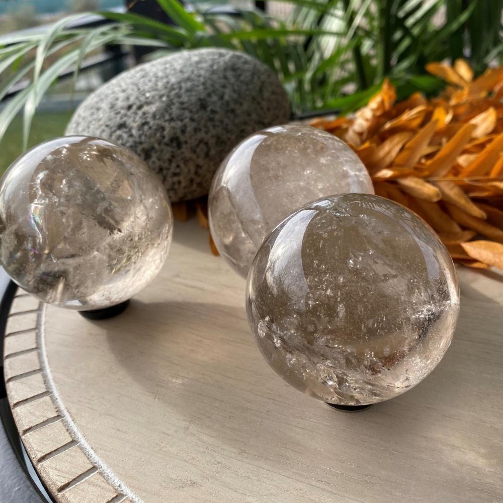 Three polished smoky quartz spheres side by side, each with its own shade of brown and inner veils