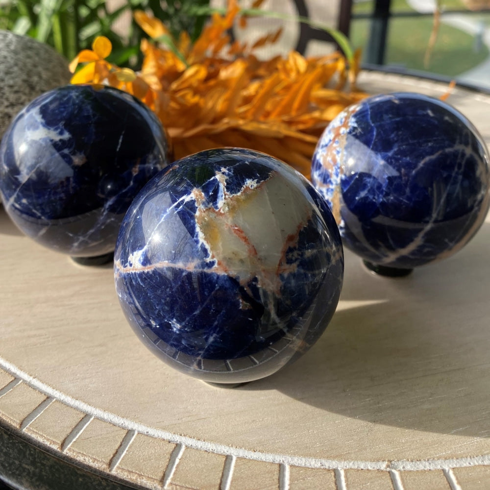 Three polished sodalite spheres on a tray, each with its own pattern of white, cream and peach veins through deep blue