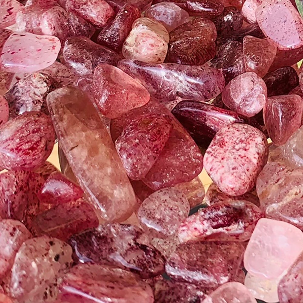 Close-up of tumbled strawberry quartz showing the tiny red speckled inclusions inside each pink stone